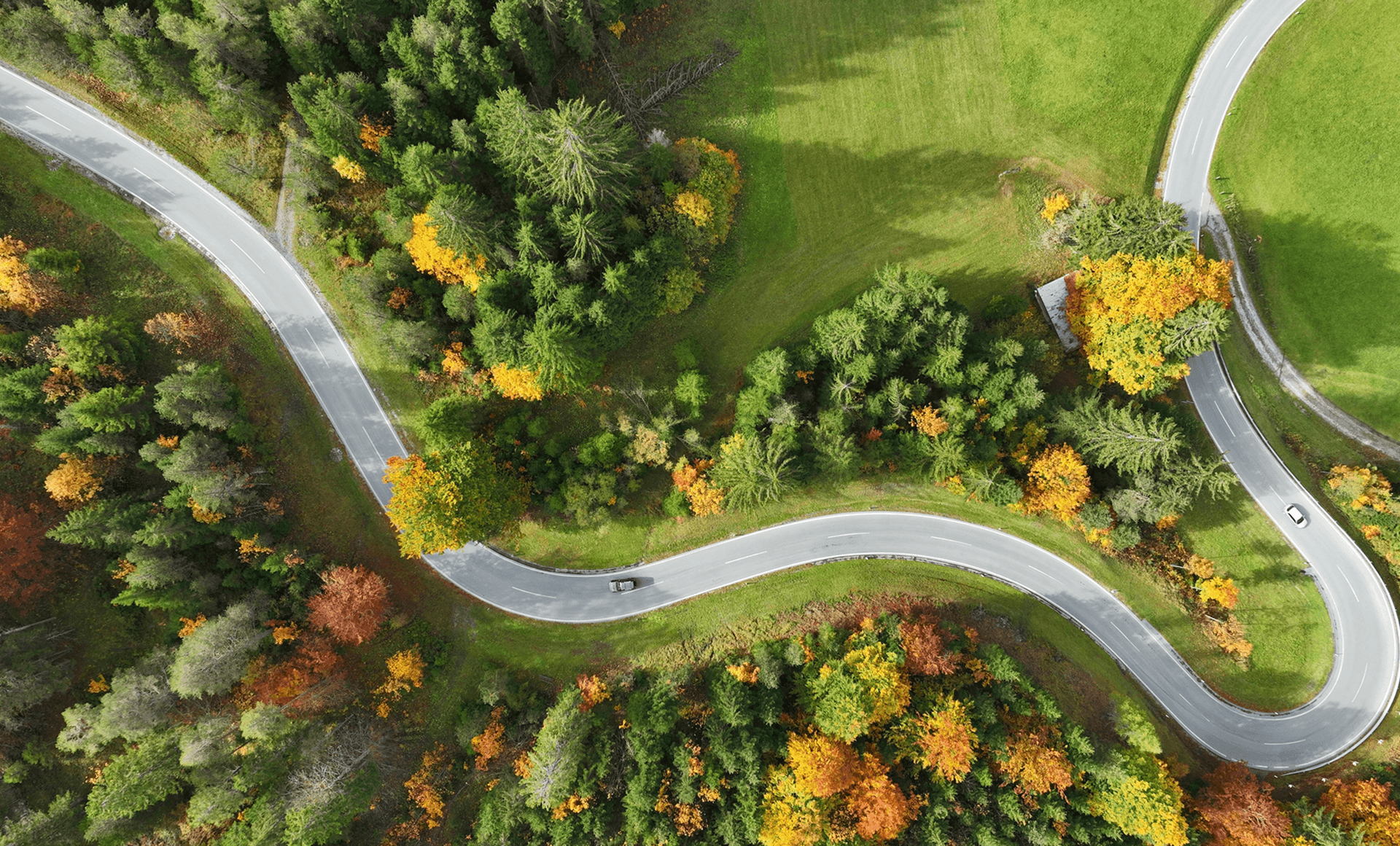 Aerial view of a winding country road cutting through fall forests and meadows.