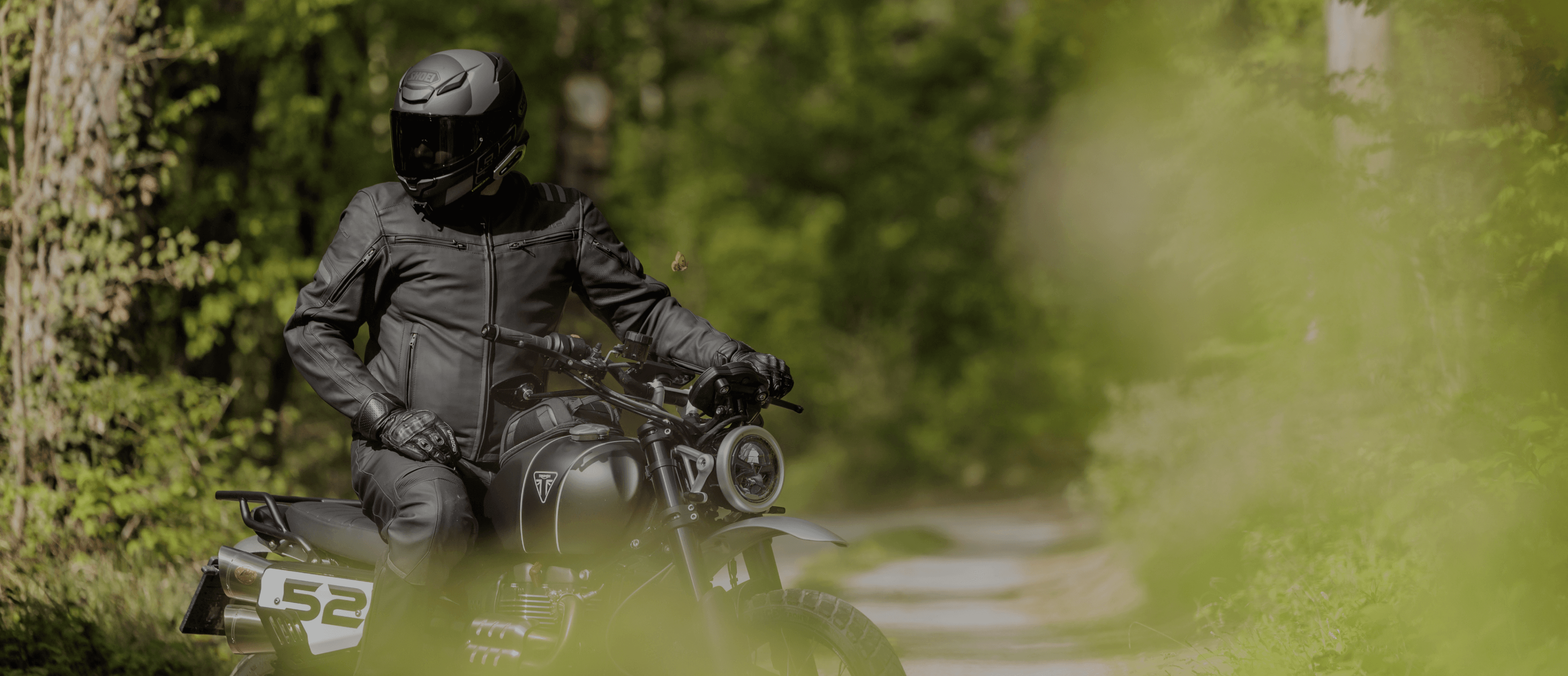 Rider on a Triumph on a twisty forest road with app display and “Turn every ride<br>
<b>into an adventure</b>.”
