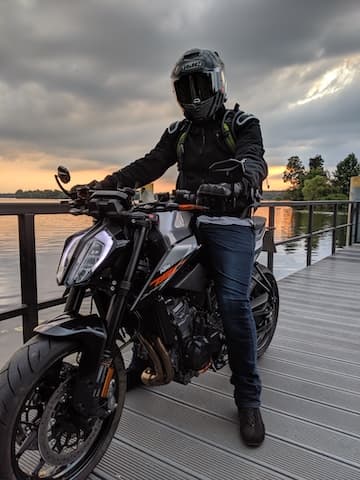 Motorradfahrer genießt den Sonnenuntergang am Wasser – Pause auf einer malerischen Motorradtour mit der perfekten Motorradnavigation.