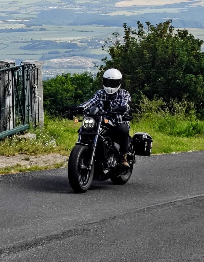 Motorradfahrer fährt auf einer kurvigen Landstraße durch malerische Hügel – entdecke solche schönen Landschaften mit unserer Motorradnavigation.